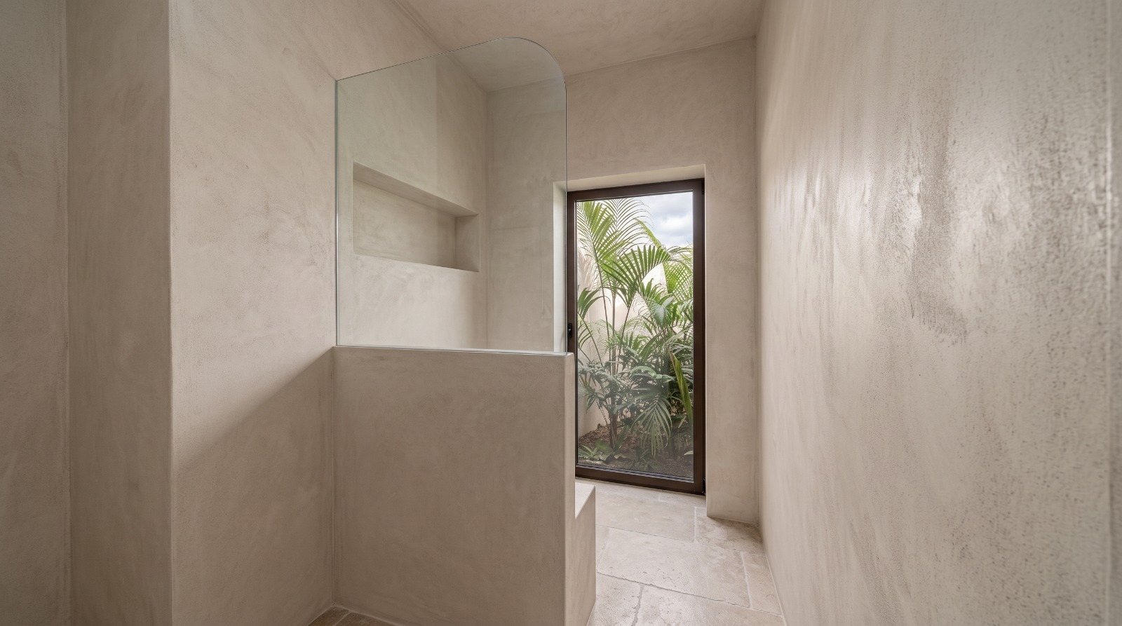 Plastered shower with a curved glass screen and a door onto a planted patio.