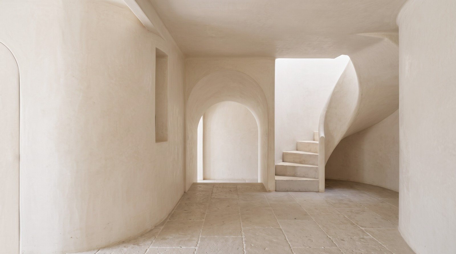 Curved plaster walls, an arched doorway and a sculpted staircase, all in warm white.