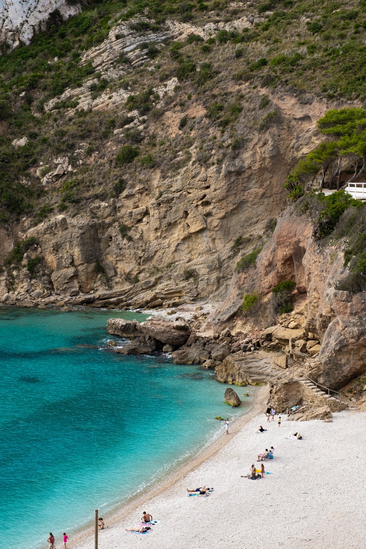 The pebble beach of La Granadella at the foot of the cliff, with a few bathers.