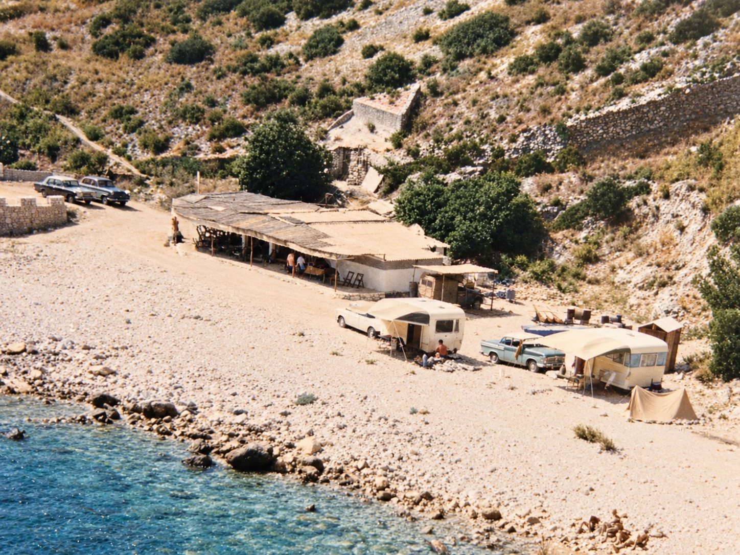 Old photograph: the pebble beach with a reed-roofed beach bar, vintage cars, caravans and a tent.